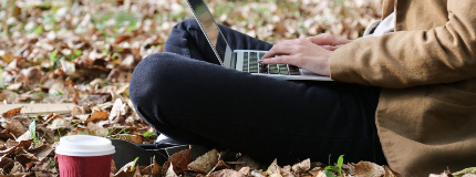 person sitting outside in fall on their computer